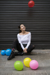 Junge Frau sitzt auf dem Bürgersteig und beobachtet einen fliegenden Ballon - KKAF00651