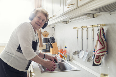 Porträt einer älteren Frau, die beim Abwasch mit Kopfhörern Musik hört - FRF00503