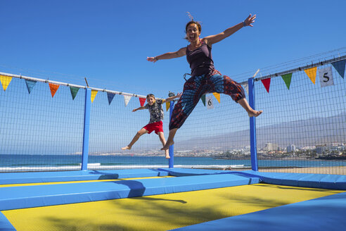 Verspielte Mutter und Sohn hüpfen auf dem Trampolin an der Küste - SIPF01624