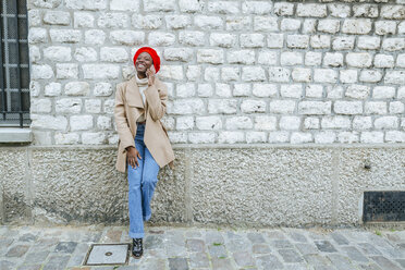 Young woman in Paris leaning against wall and talking on the phone - KIJF01358