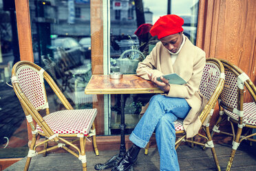 Young woman in Paris reading menu in a cafe - KIJF01366