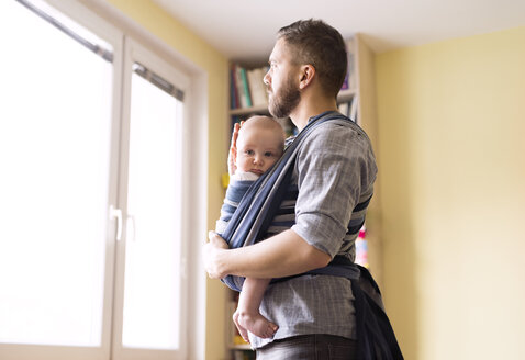 Vater mit Baby im Tragetuch zu Hause und Blick aus dem Fenster - HAPF01413