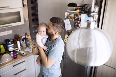 Father holding and kissing baby son in kitchen - HAPF01437