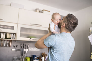 Father holding and kissing baby son in kitchen - HAPF01439