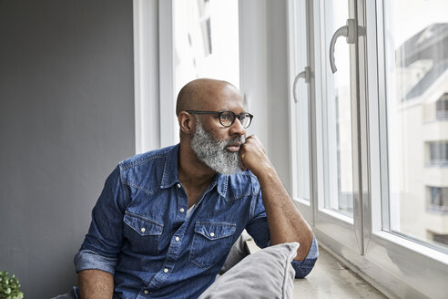 Mature man sitting at window, looking worried - FMKF03731