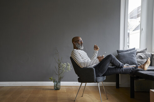 Mature man sitting with feet up, using smartphone - FMKF03745