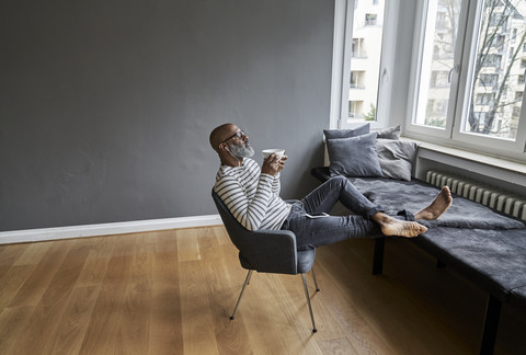 Matureman with earphones sitting at window, drinking coffee stock photo