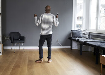 Mature man dancing alone at home, holding smart phone - FMKF03752