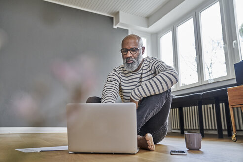 Älterer Mann sitzt auf dem Boden und arbeitet am Laptop - FMKF03756