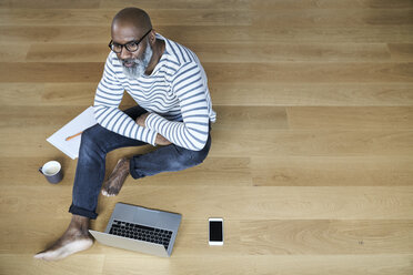 Mature man sitting on floor, working on laptop - FMKF03758