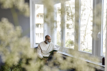 Älterer Mann sitzt am Fenster und liest ein Buch - FMKF03761