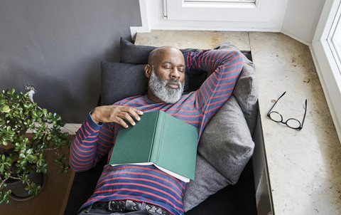 Matur man lying on bench with a book, taking a nap stock photo