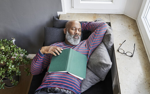 Matur man lying on bench with a book, taking a nap - FMKF03764