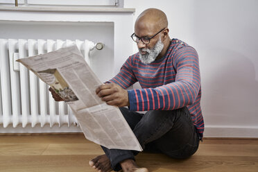 Älterer Mann sitzt auf dem Boden und liest Zeitung - FMKF03766