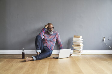 Mature man sitting on floor, using laptop - FMKF03770