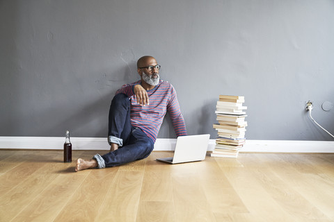 Älterer Mann sitzt auf dem Boden und benutzt einen Laptop, lizenzfreies Stockfoto