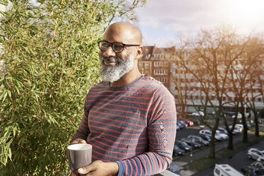 Mature amn standing on balcony, drinking coffee - FMKF03780