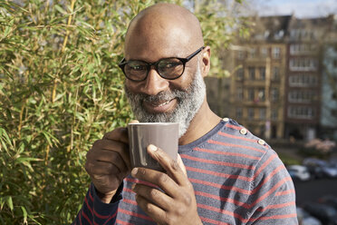 Mature amn standing on balcony, drinking coffee - FMKF03781