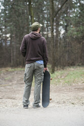 Rückansicht eines stehenden Mannes, der ein Skateboard hält - MOMF00048