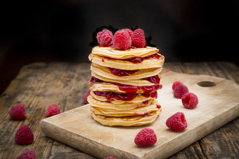 Stack of pancakes with raspberries and raspberry jam on wooden board stock photo