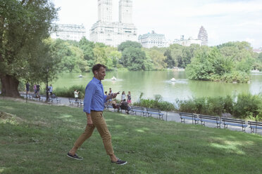 USA, Manhattan, Central Park, Mann geht mit Handy und Kopfhörern auf einer Wiese spazieren - BOYF00755