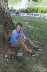 Mann sitzend auf einer Wiese in einem Park mit Notizbuch - BOYF00764