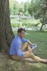 Mann mit Mini-Tablet sitzend auf einer Wiese in einem Park - BOYF00771