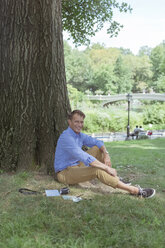 Smiling man relaxing on a meadow in a park - BOYF00773