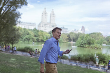 USA, Manhattan, Central Park, lächelnder Mann mit Mobiltelefon und Kopfhörern - BOYF00775