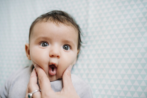 Baby with funny face, mother's Hand pressing her cheek - GEMF01578