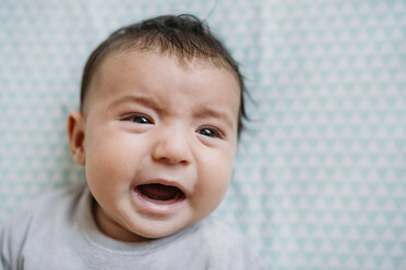 Portrait of crying baby girl lying on bed - GEMF01580