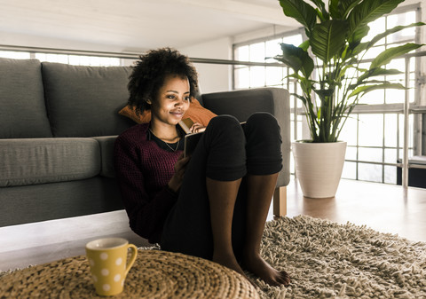 Smiling young woman at home holding credit card and tablet stock photo