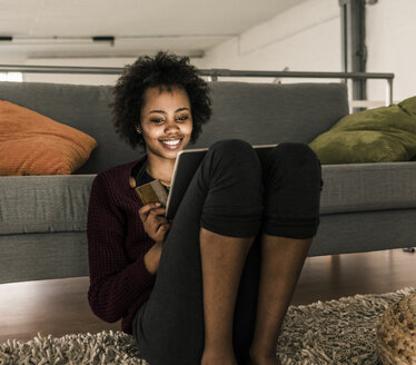 Smiling young woman at home holding credit card and tablet - UUF10317