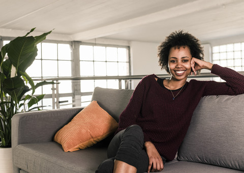 Porträt einer lächelnden jungen Frau, die auf einer Couch sitzt, lizenzfreies Stockfoto