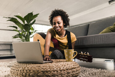 Lächelnde junge Frau zu Hause mit Gitarre und Laptop - UUF10322