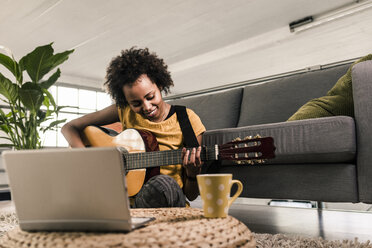 Smiling young woman at home with laptop playing guitar - UUF10324