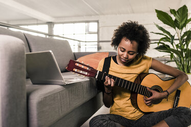 Young woman at home with laptop playing guitar - UUF10325