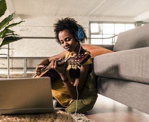 Junge Frau zu Hause mit Kopfhörern und Laptop spielt Gitarre - UUF10326
