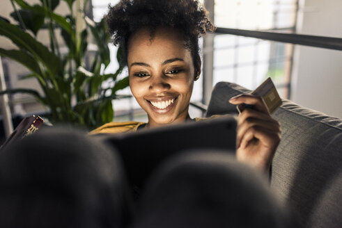 Smiling young woman on couch with credit card and laptop - UUF10335