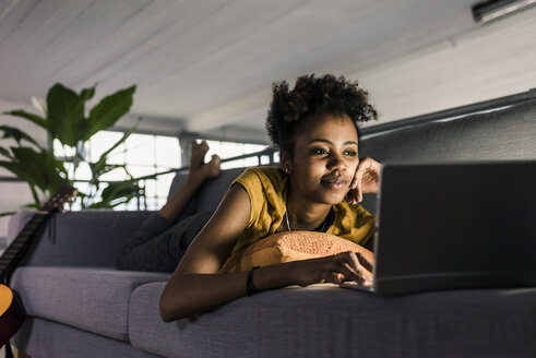 Junge Frau auf der Couch liegend mit Laptop - UUF10337