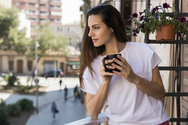 Frau mit Kaffeetasse auf dem Balkon stehend und in die Ferne blickend - KKAF00659