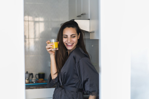 Porträt einer lachenden jungen Frau mit einem Glas Orangensaft in der Küche, lizenzfreies Stockfoto
