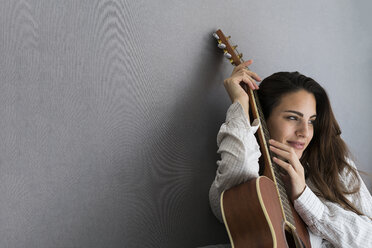 Portrait of smiling young woman with guitar in front of grey background - KKAF00677