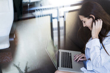 Smiling young woman sitting on balcony using laptop - KKAF00686