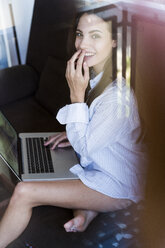 Porträt einer lächelnden jungen Frau, die auf einem Balkon sitzt und einen Laptop benutzt - KKAF00687