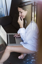 Smiling young woman sitting on balcony using laptop - KKAF00688