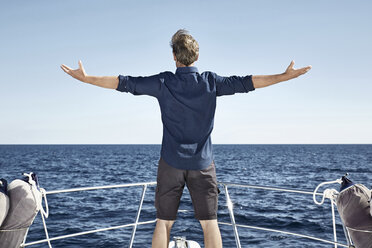 Back view of mature man standing on his motor yacht with arms outstretched - PDF01112
