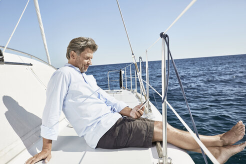 Älterer Mann sitzt auf seinem Segelboot und schaut auf sein Mobiltelefon - PDF01139