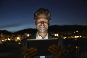 Portrait of smiling mature man standing looking at tablet in the night - PDF01149