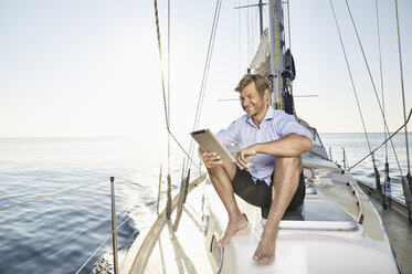 Smiling mature man sitting on his sailing boat using tablet - PDF01158
